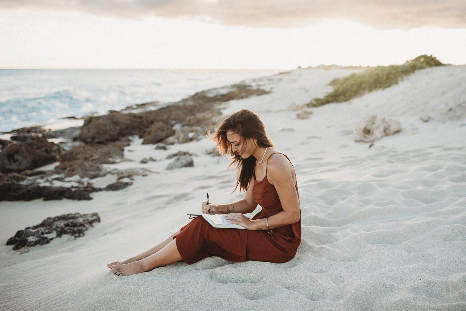 young copywriter sitting at a beach writing in a notebook