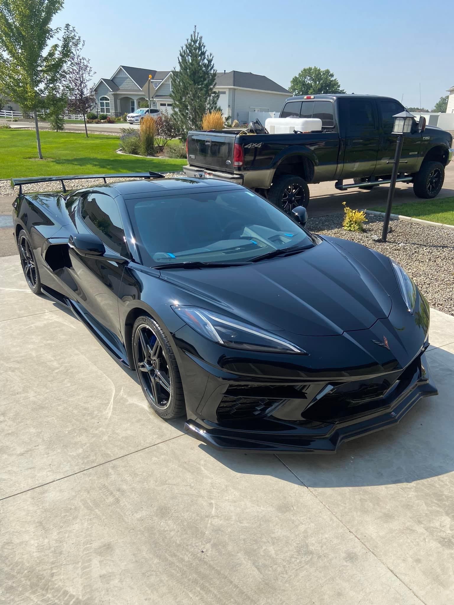 A black sports car is parked in a driveway next to a truck.