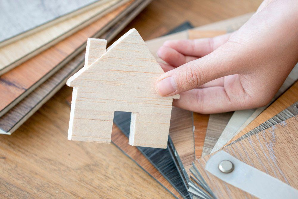 A Person Is Holding A Small Wooden House In Their Hand — Cabonne Carpets In Molong, NSW