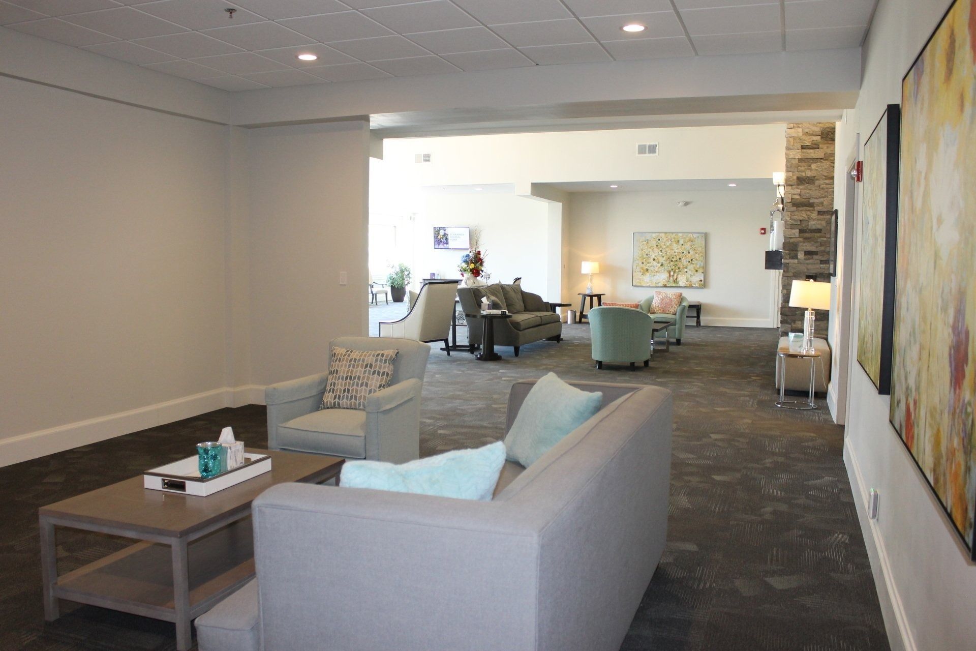 Interior of a senior living lounge with seating, artwork, and fireplace. Gray and neutral tones.