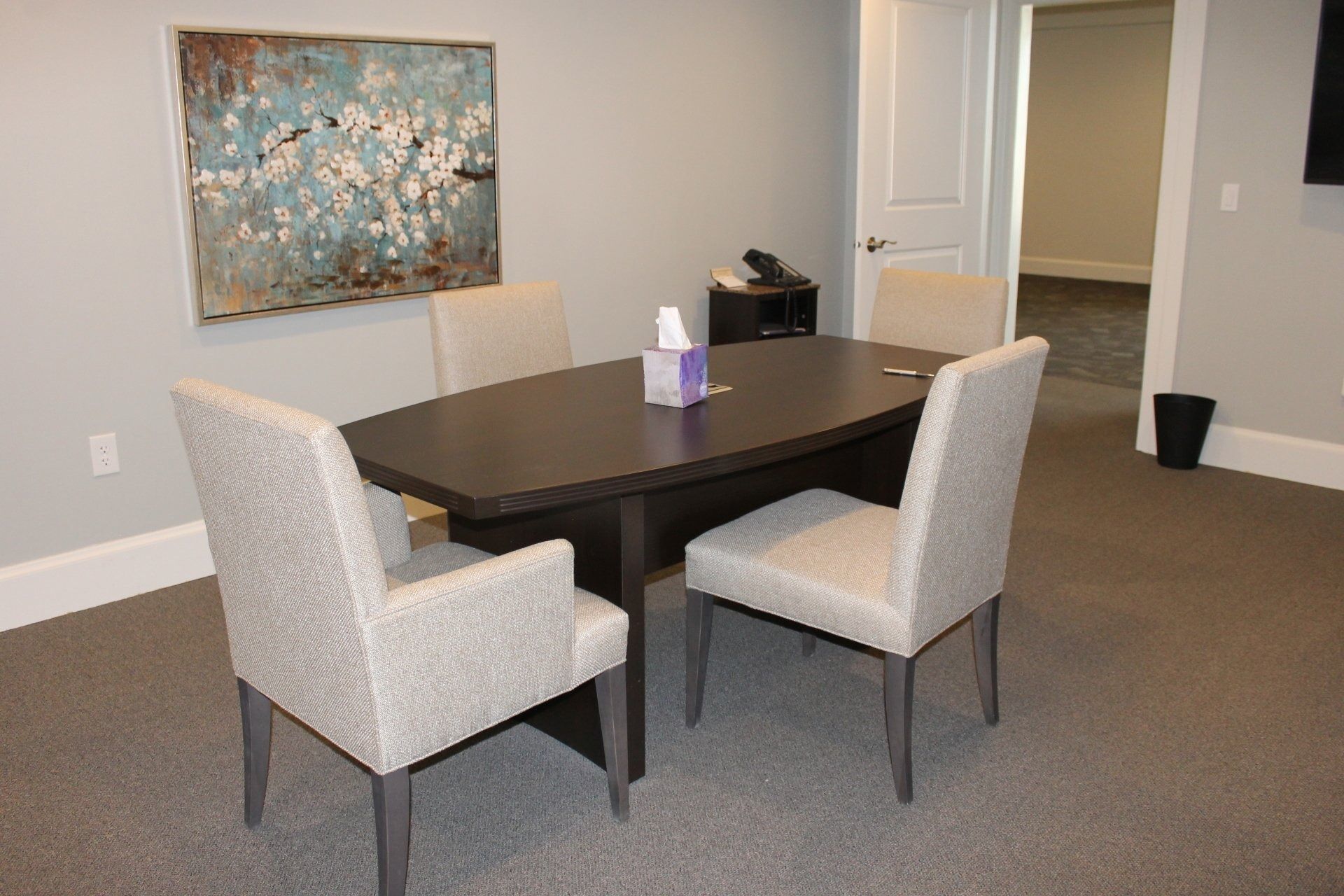 Meeting room with dark table, four chairs, artwork, and tissue box on the table.