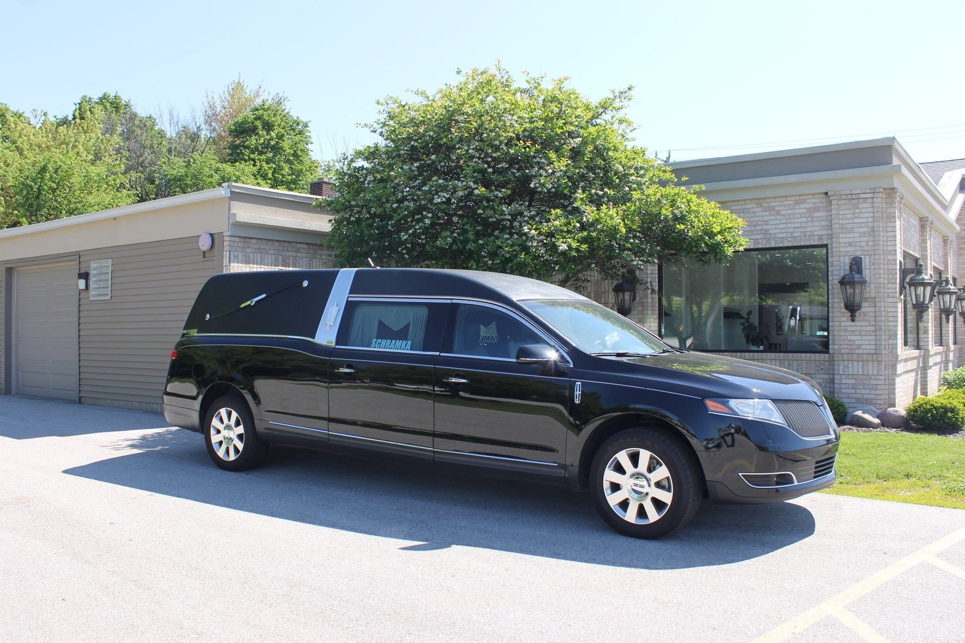 Black hearse parked outside a light-colored funeral home building, under a sunny sky.