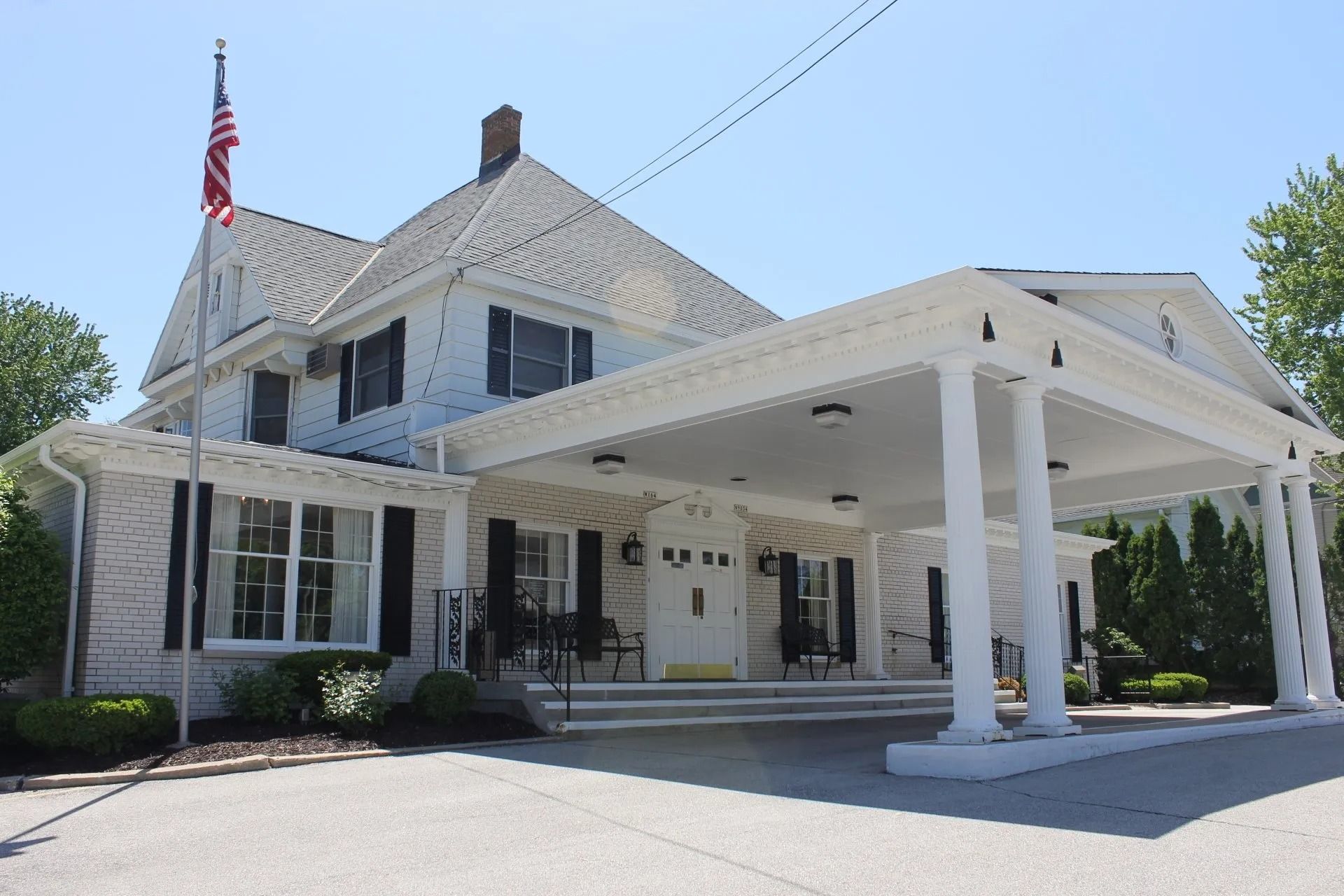 White building with columns and American flag. Porch with awning over entrance. Sunny day.