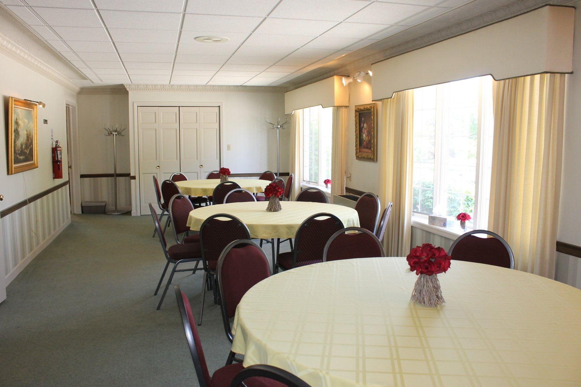 A room with round tables, chairs, and flowers. Neutral-toned walls, ceiling, and curtains.