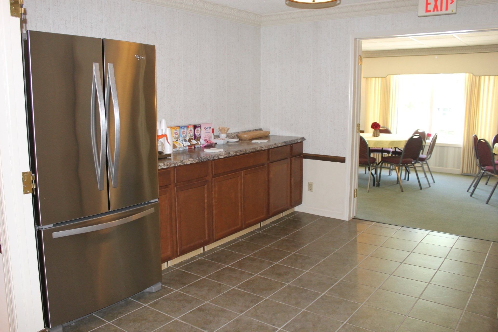 Stainless steel refrigerator next to a dark wood cabinet. A doorway leads to a dining area.