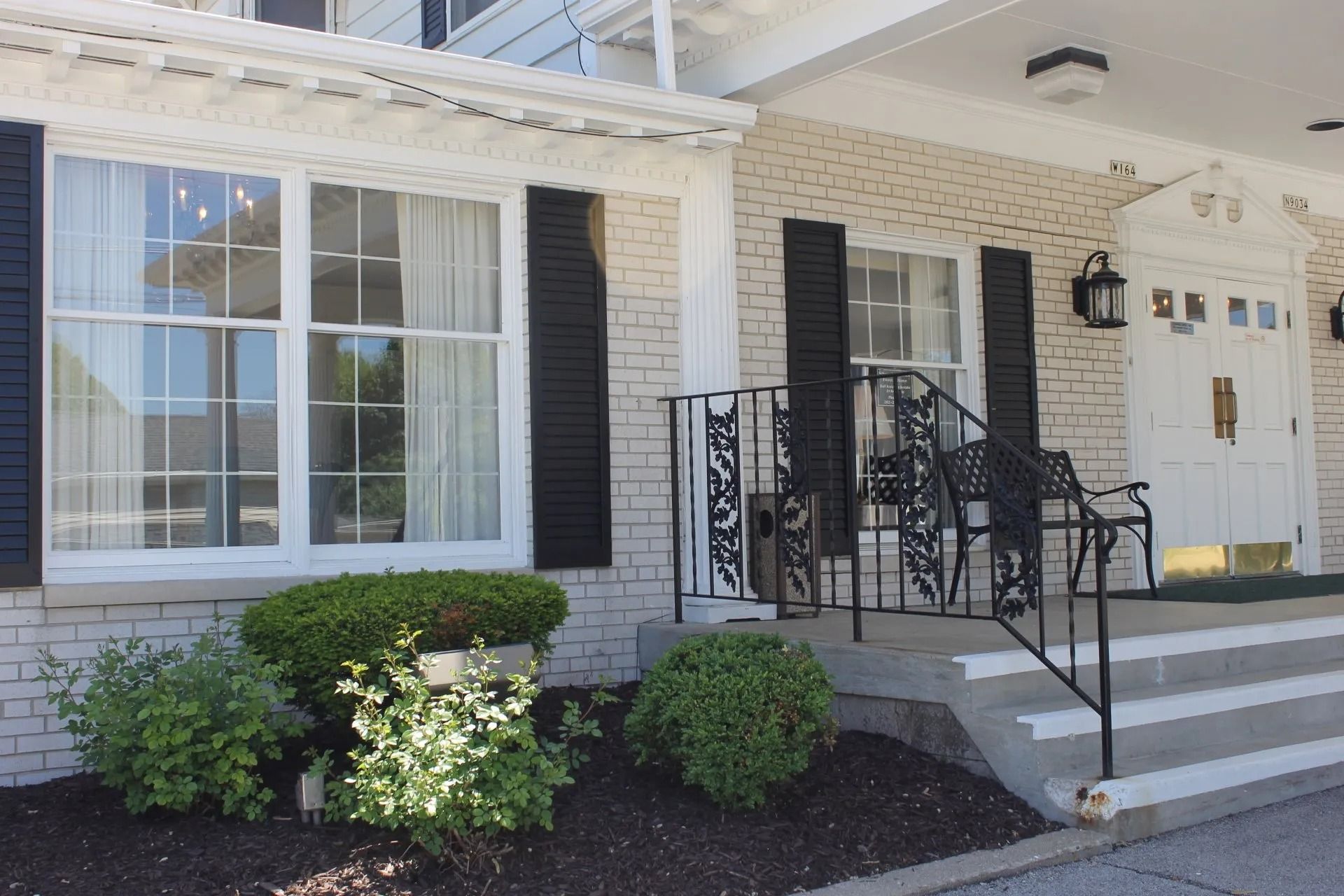 White brick building with black shutters, entrance steps, and decorative iron railing.