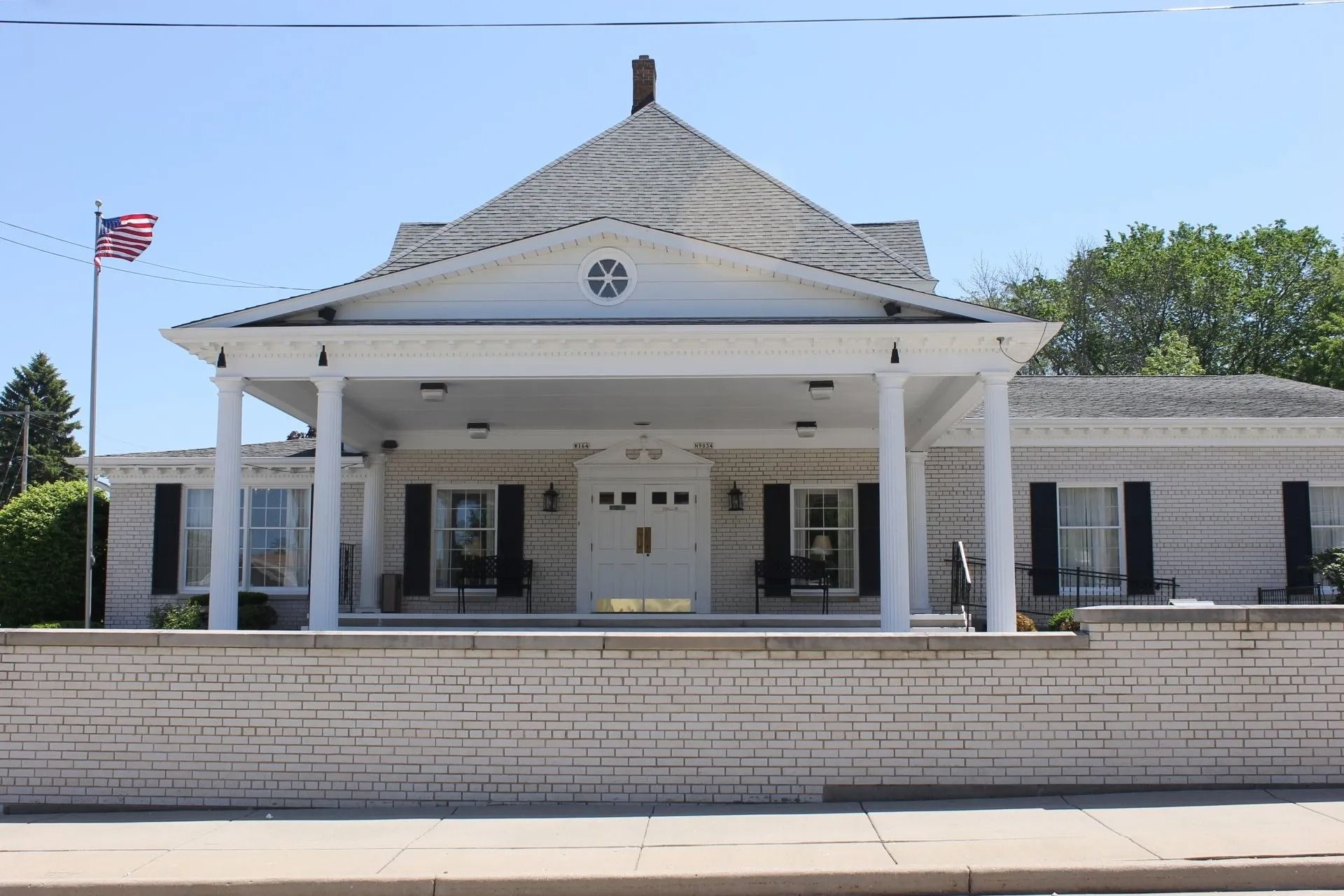 White brick building with a porch, a pagoda-style roof, and a U.S. flag flying outside.