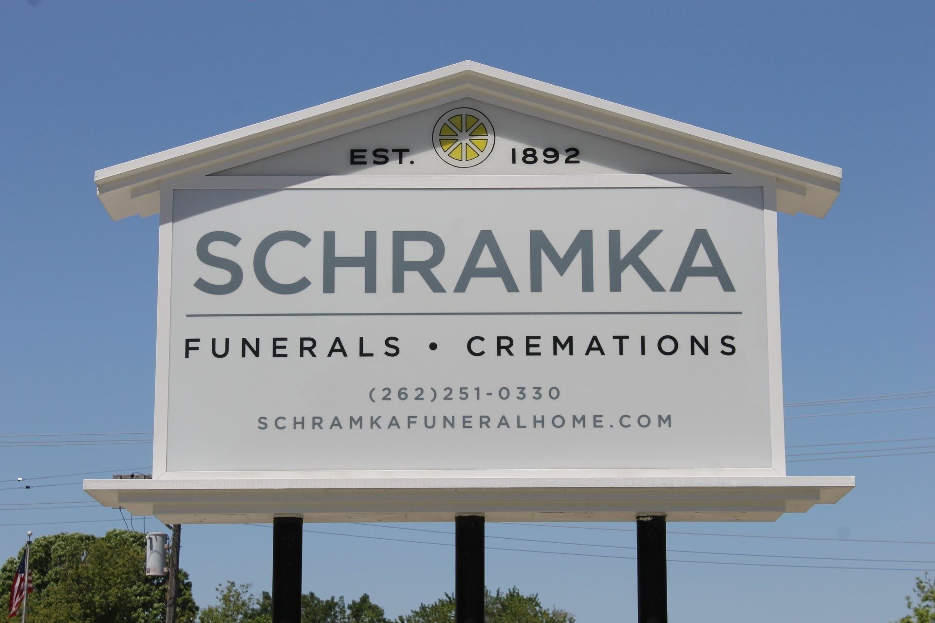 Sign for Schramka Funeral Home, white with black text, under a blue sky.