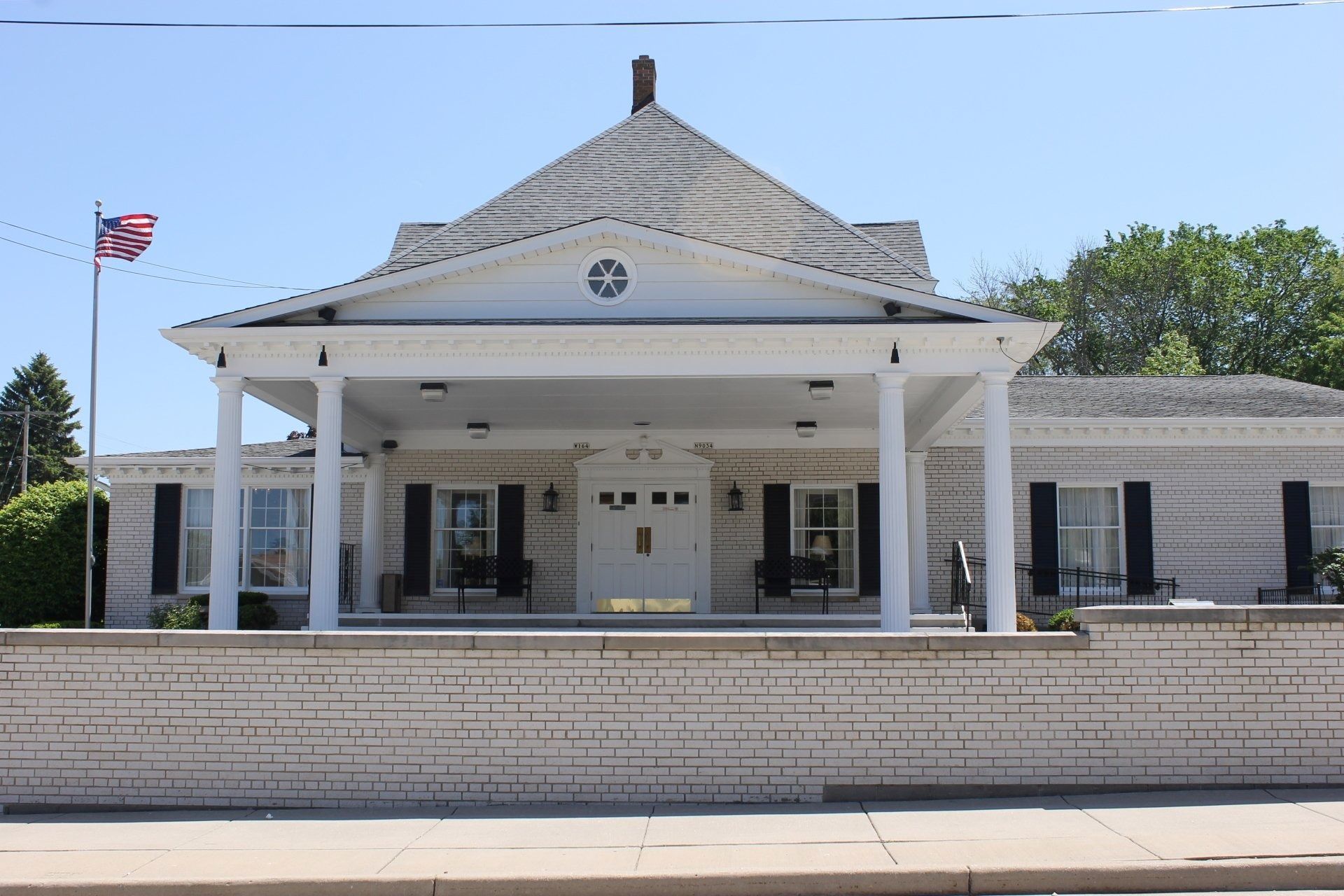White brick building with a covered entrance, a flagpole, and a light blue sky.