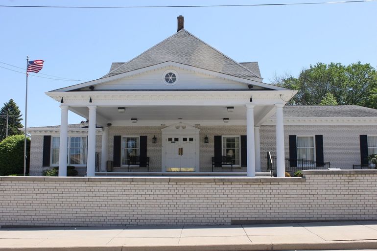 White brick building with a covered entrance, a flagpole, and a light blue sky.