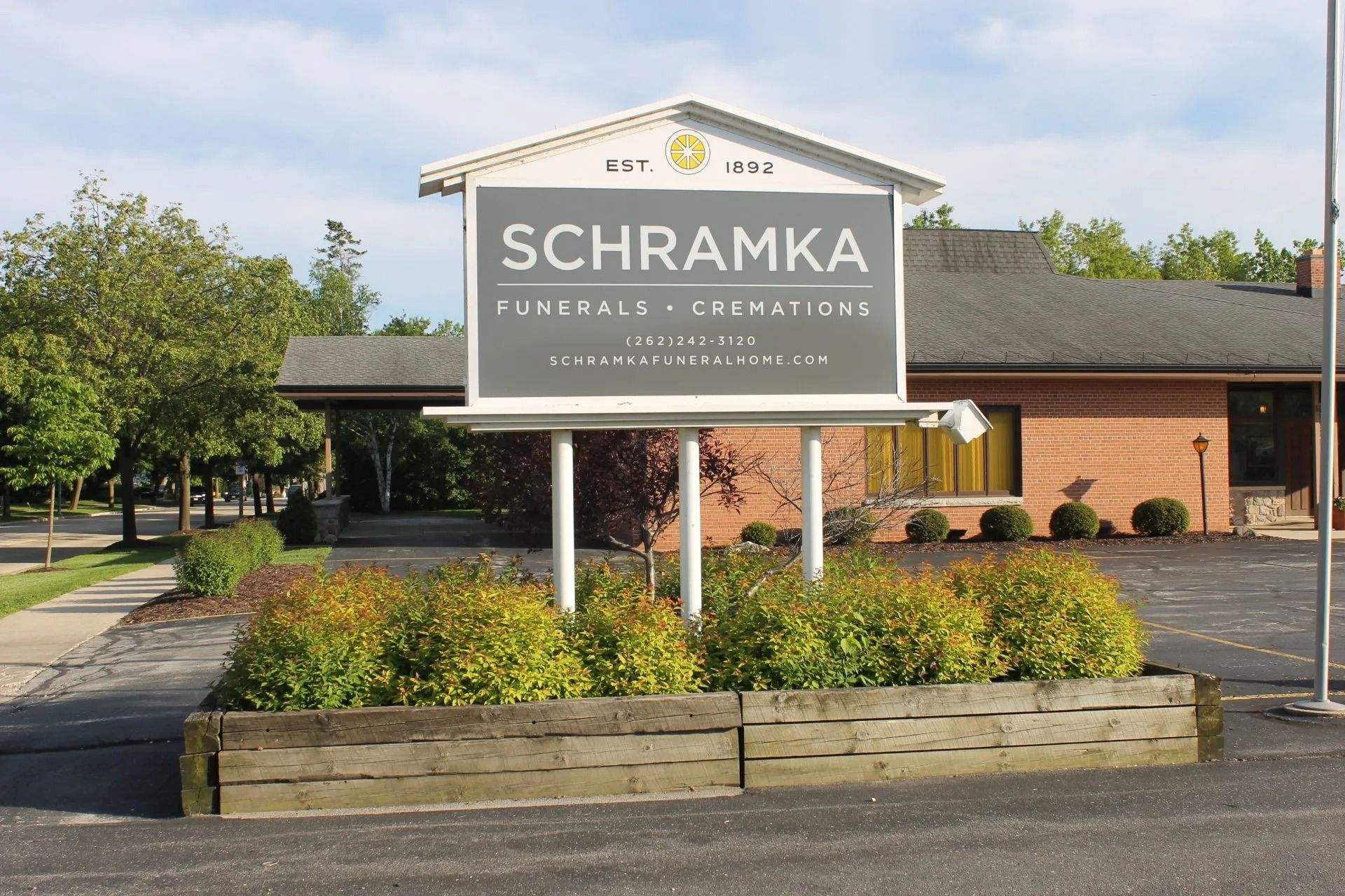 Sign for Schramka Funeral Home and Cremations, with a brick building in the background.