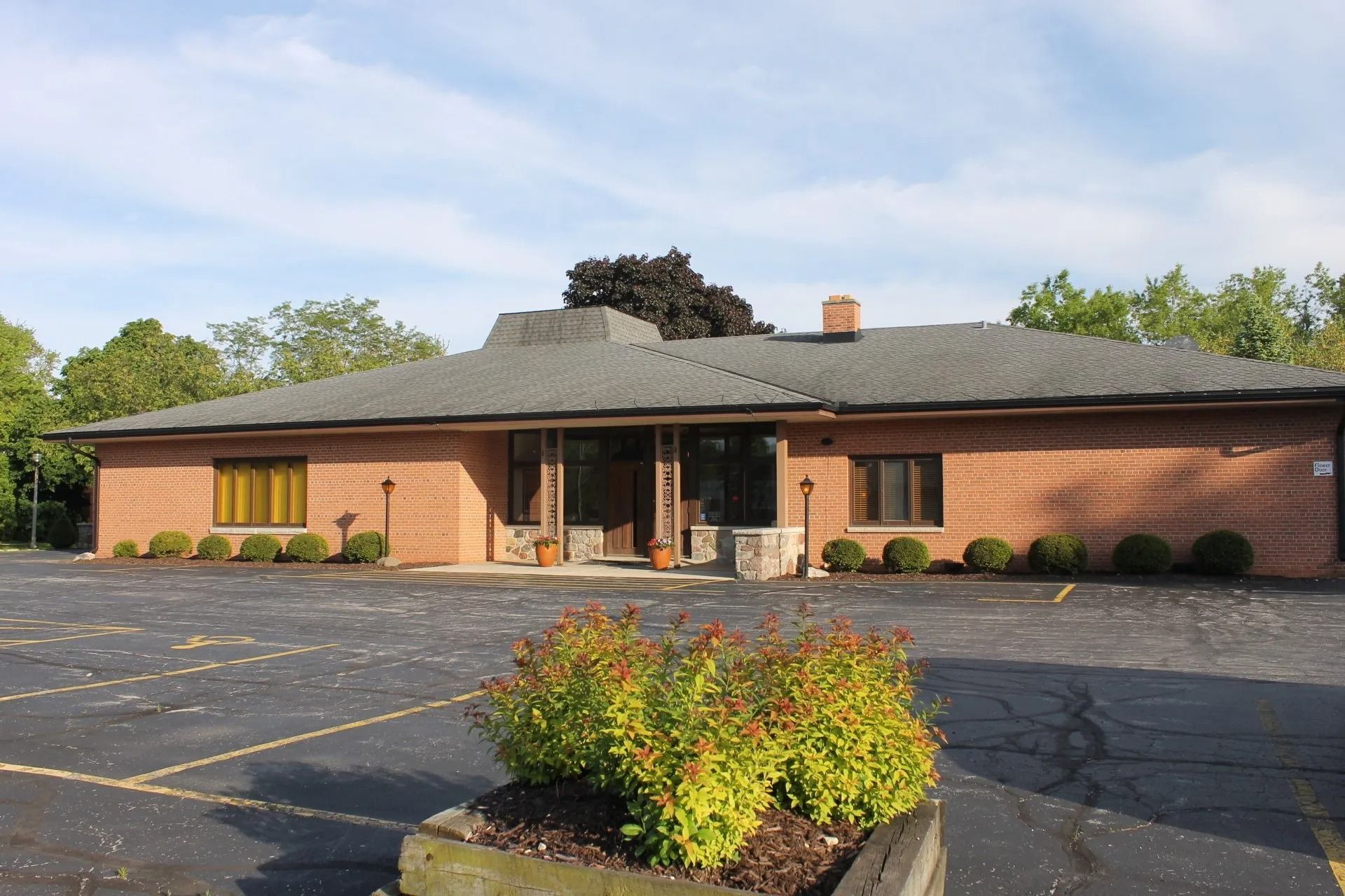 A low, brick building with a flat roof and surrounding parking lot, under a blue sky.