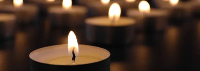 Close-up of lit candles in the dark, some in focus, with soft warm glow and blurred background.