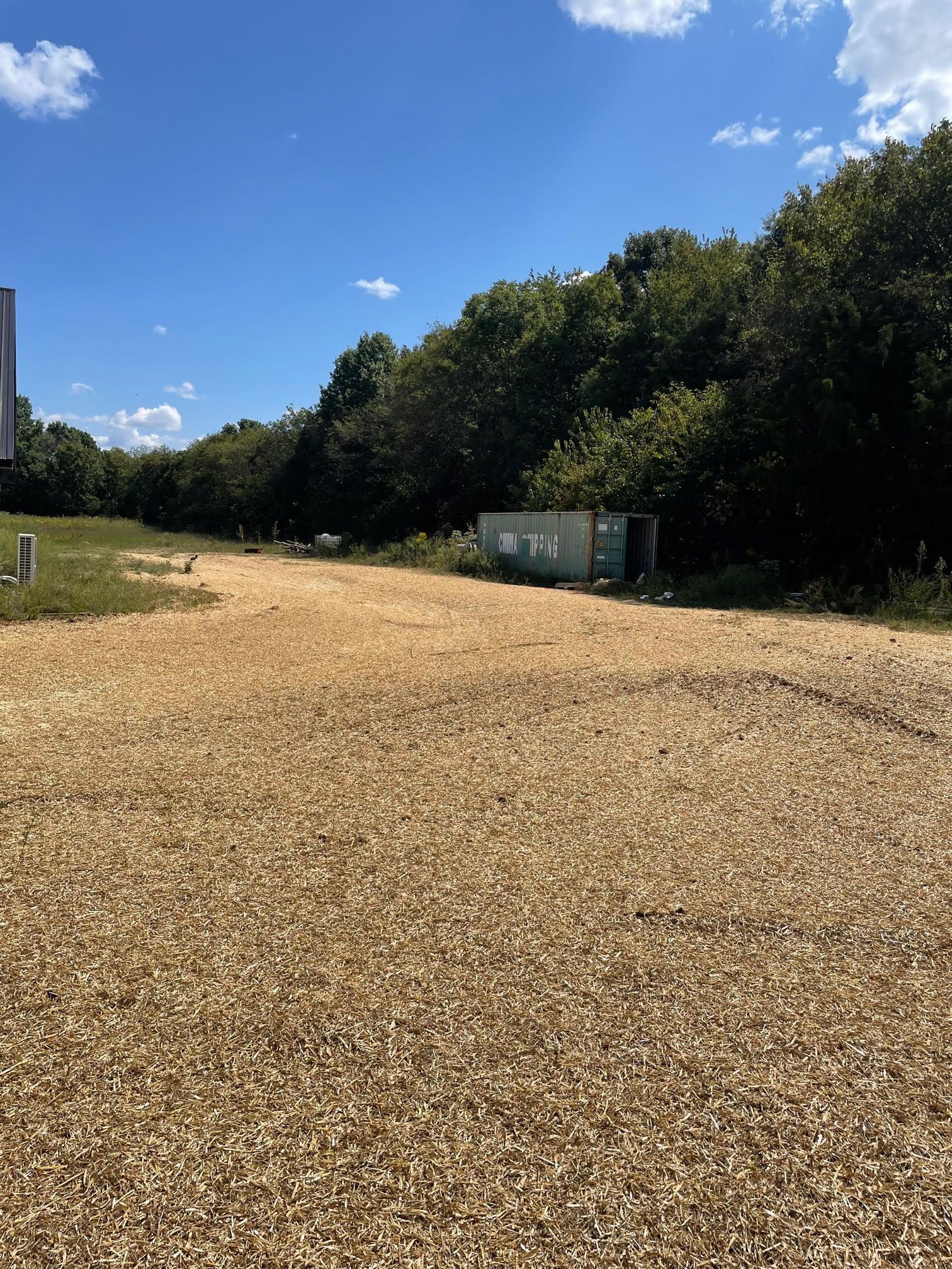 A gravel road going through a field with trees in the background.