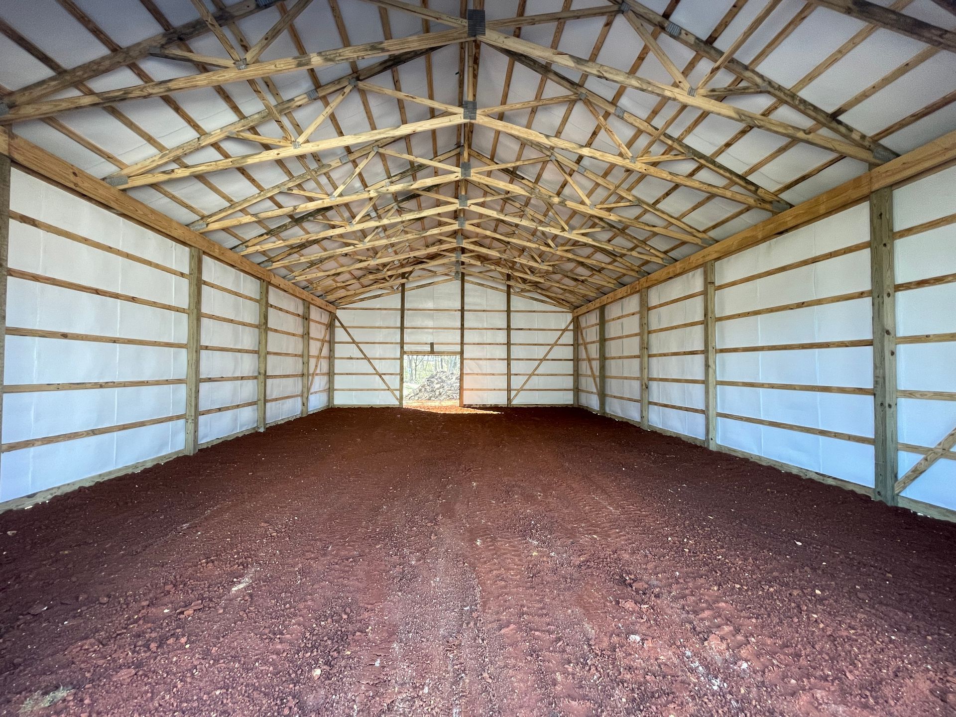 Interior of a large barn with dirt floor and wooden framing. White walls and ceiling.