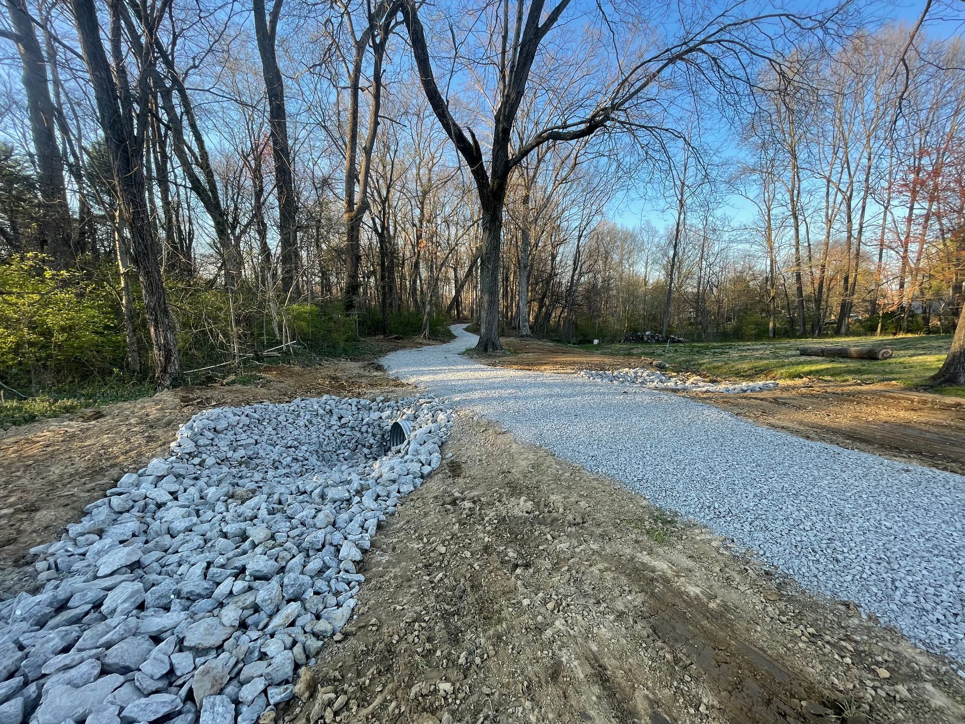 Gravel path through a wooded area, partially covered with large rocks. Overcast sky, trees in the background.