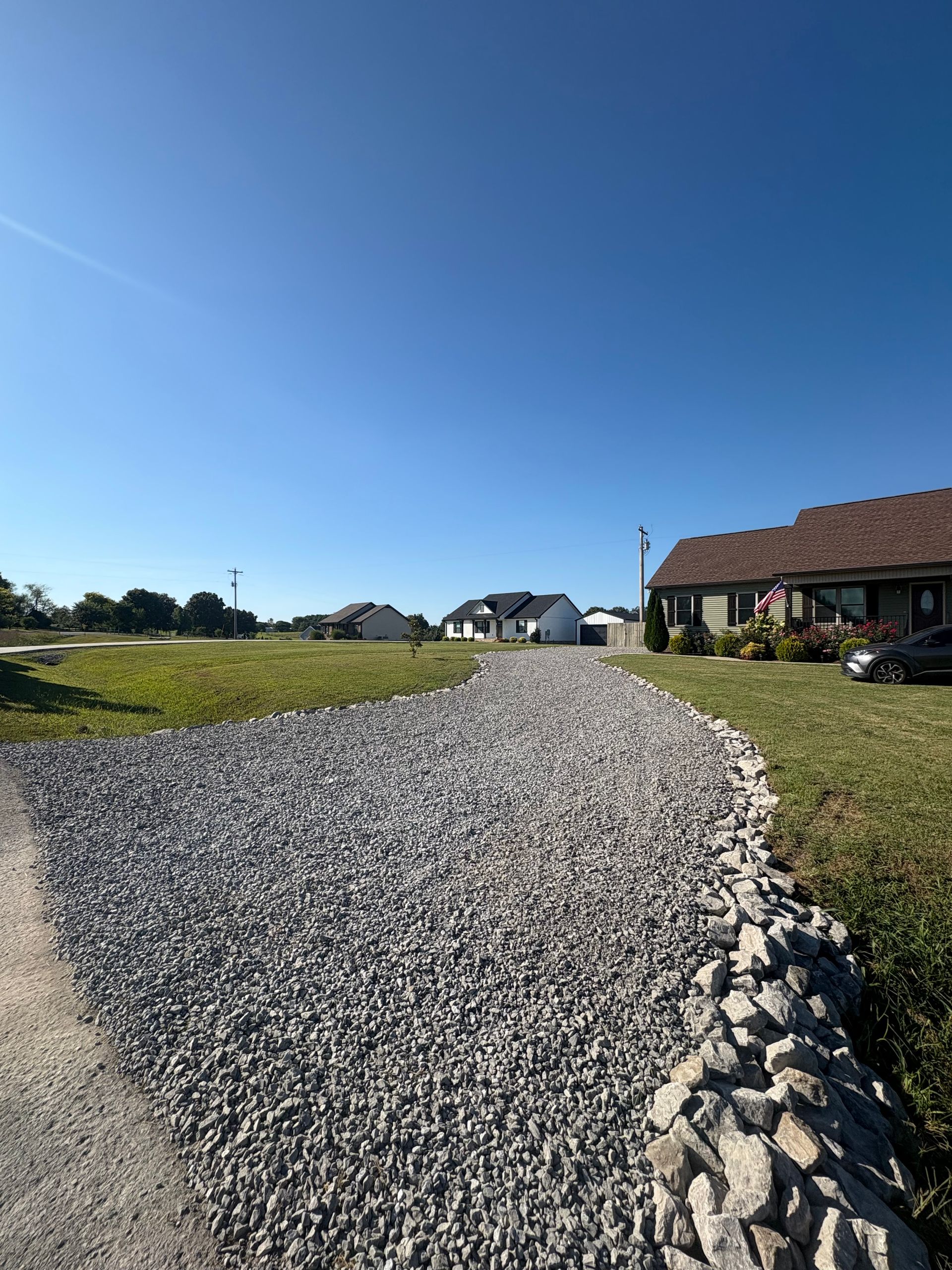 A gravel road going through a grassy field with trees in the background