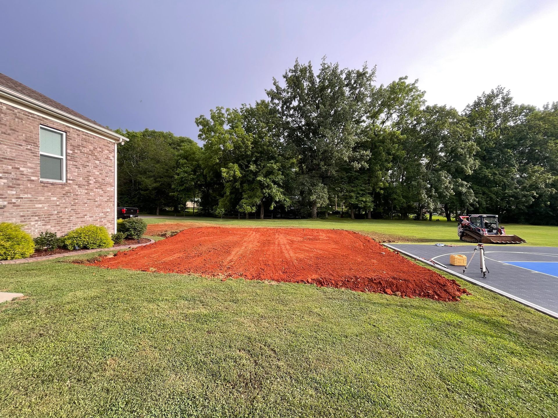 Red mulch bed prepared for planting, beside a brick house and a driveway.