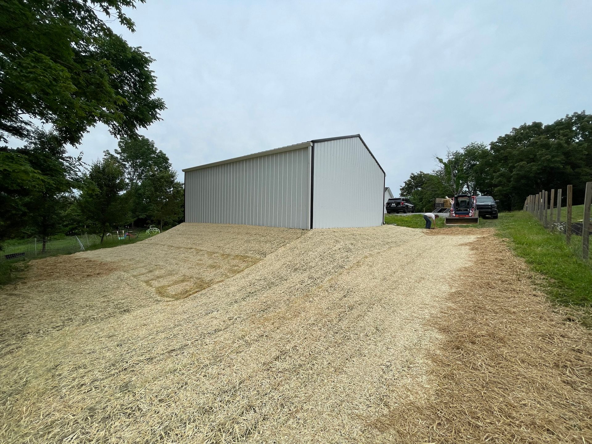 White metal building with gravel piles in front, small tractor nearby on a cloudy day.