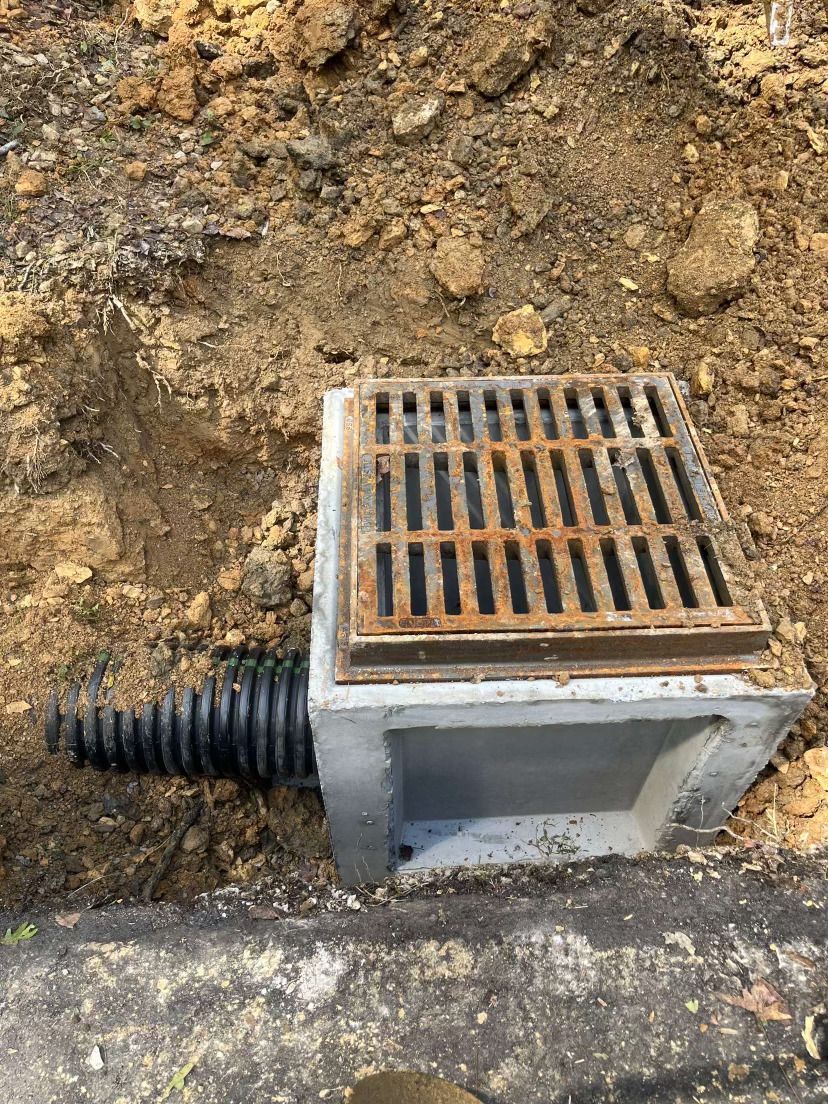 A manhole cover is sitting in the dirt next to a pipe.