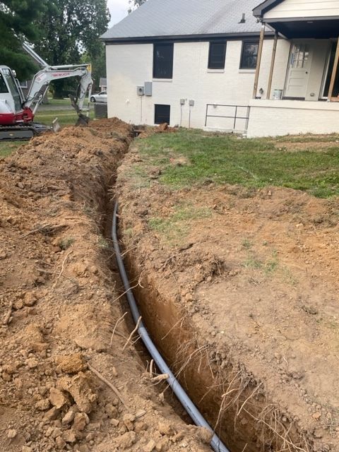 An excavator is digging a trench in front of a house