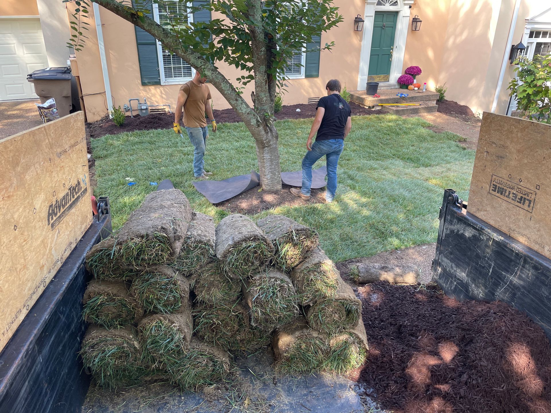 Two men are working on a lawn in front of a house.