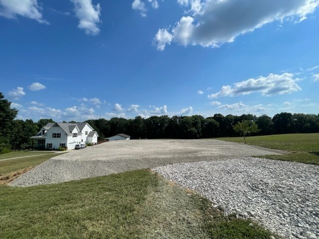 A large white house is sitting in the middle of a grassy field.