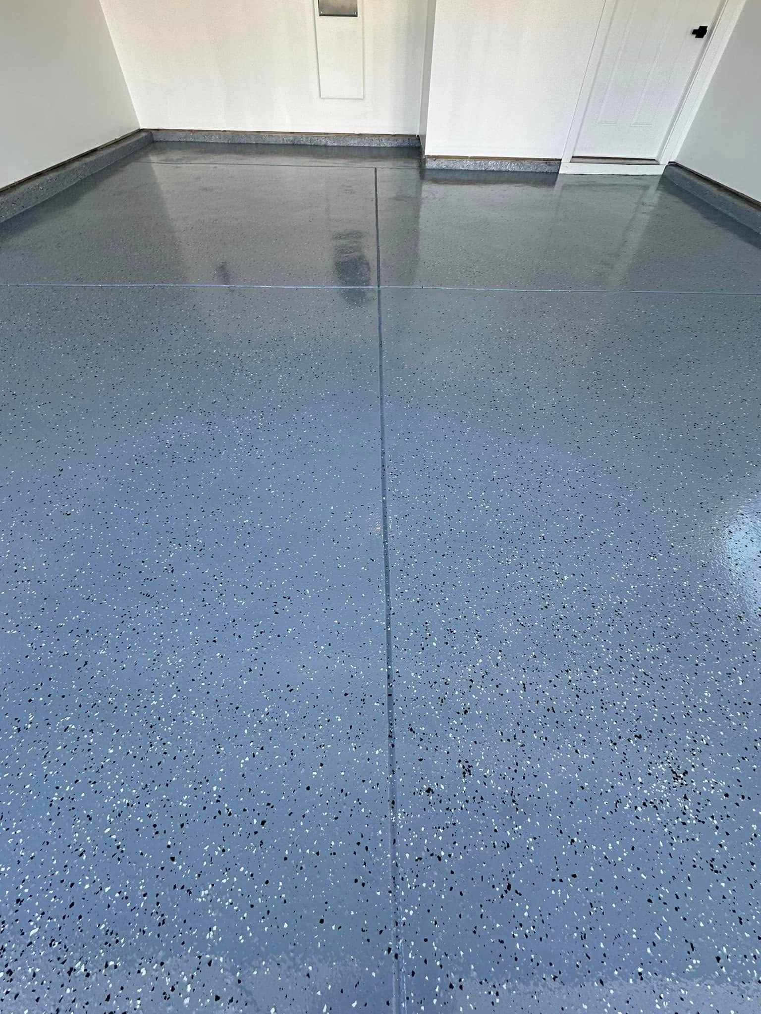 A garage floor coated in glossy, grey epoxy speckled with small black and white paint chips.