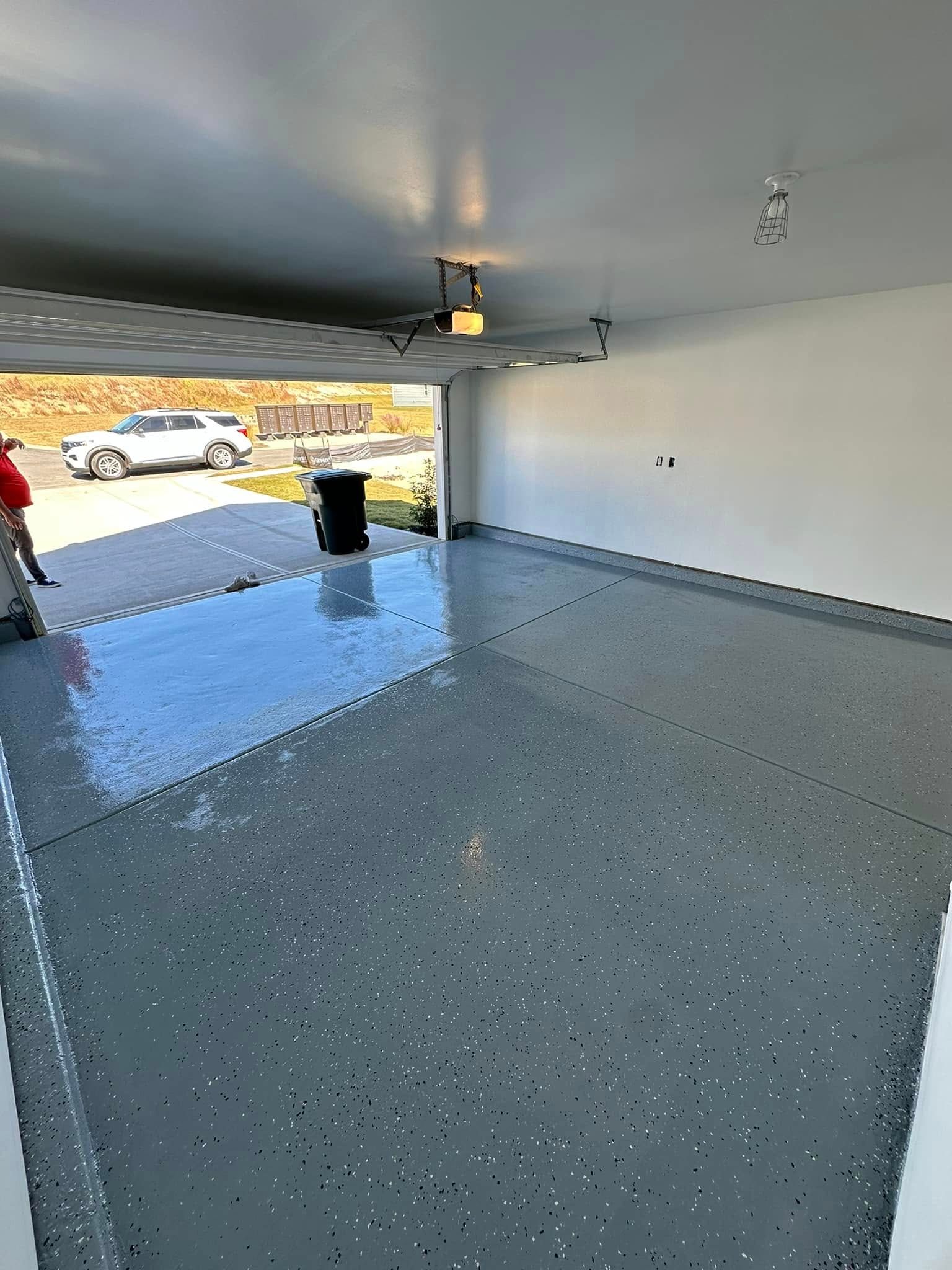 A polished, grey epoxy garage floor with black and white flakes, reflecting light inside a clean, empty garage.