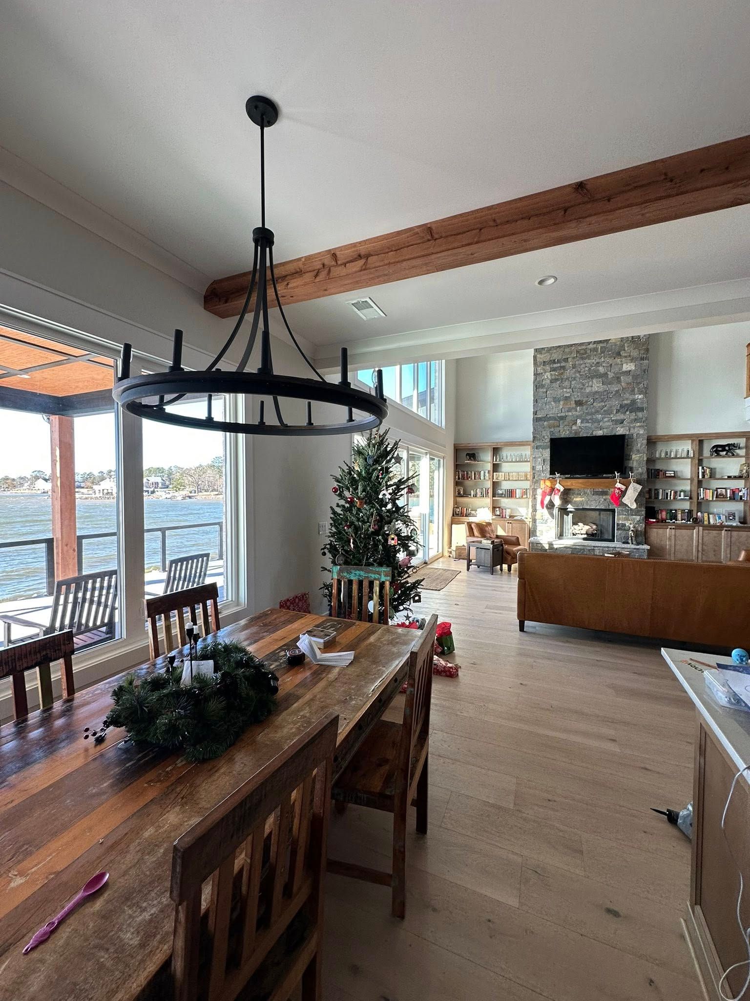 A dining area with a rustic wooden table and a large circular chandelier, looking into a living room with a stone fireplace.