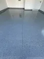 A smooth, glossy gray garage floor with a decorative speckled finish, divided by a straight expansion joint.