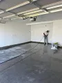 A person uses a pressure washer to clean a large, gray concrete garage floor.