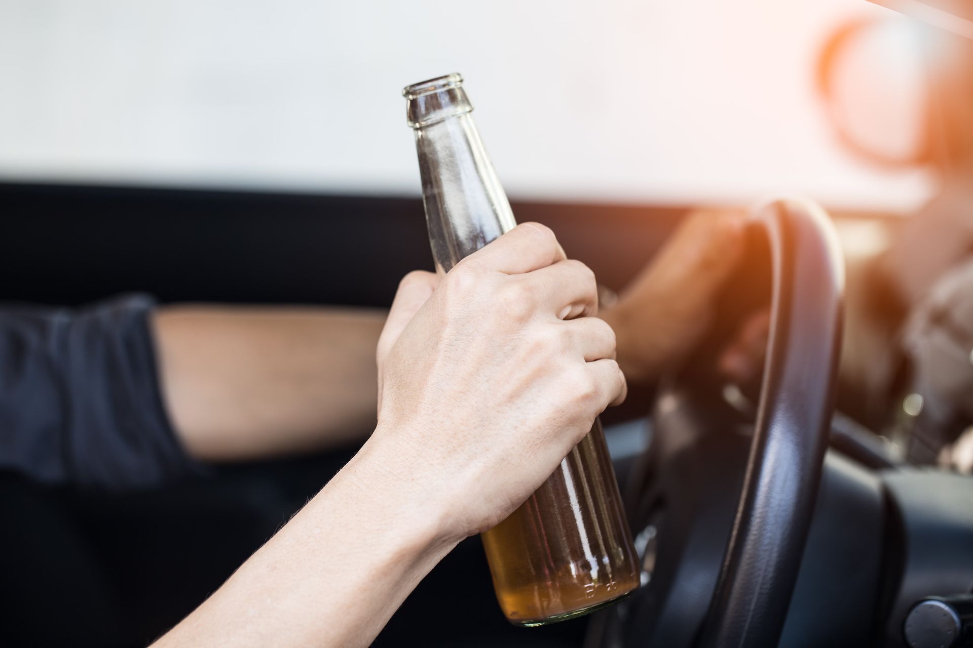 Person driving a car while holding a beer bottle, action endangering safety.