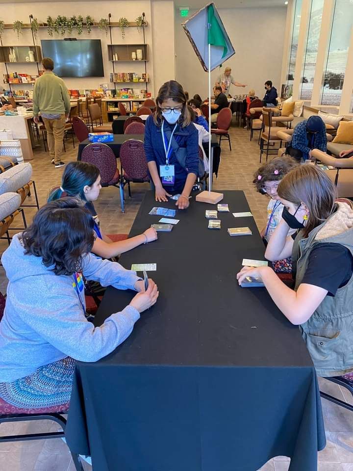 A group of people are sitting around a table playing cards at GameSchoolCon.