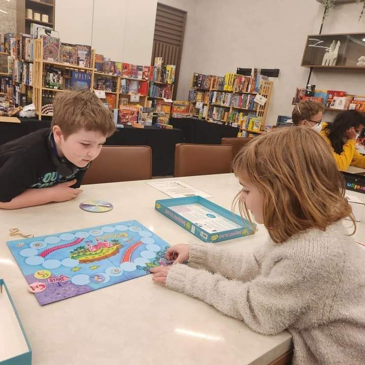 A boy and a girl are sitting at a table playing a board game at GameSchoolCon.