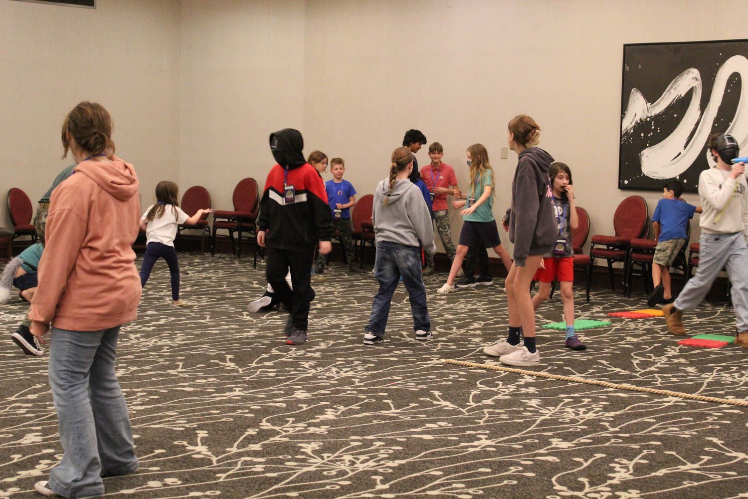 A group of children playing a game in a carpeted room with chairs.