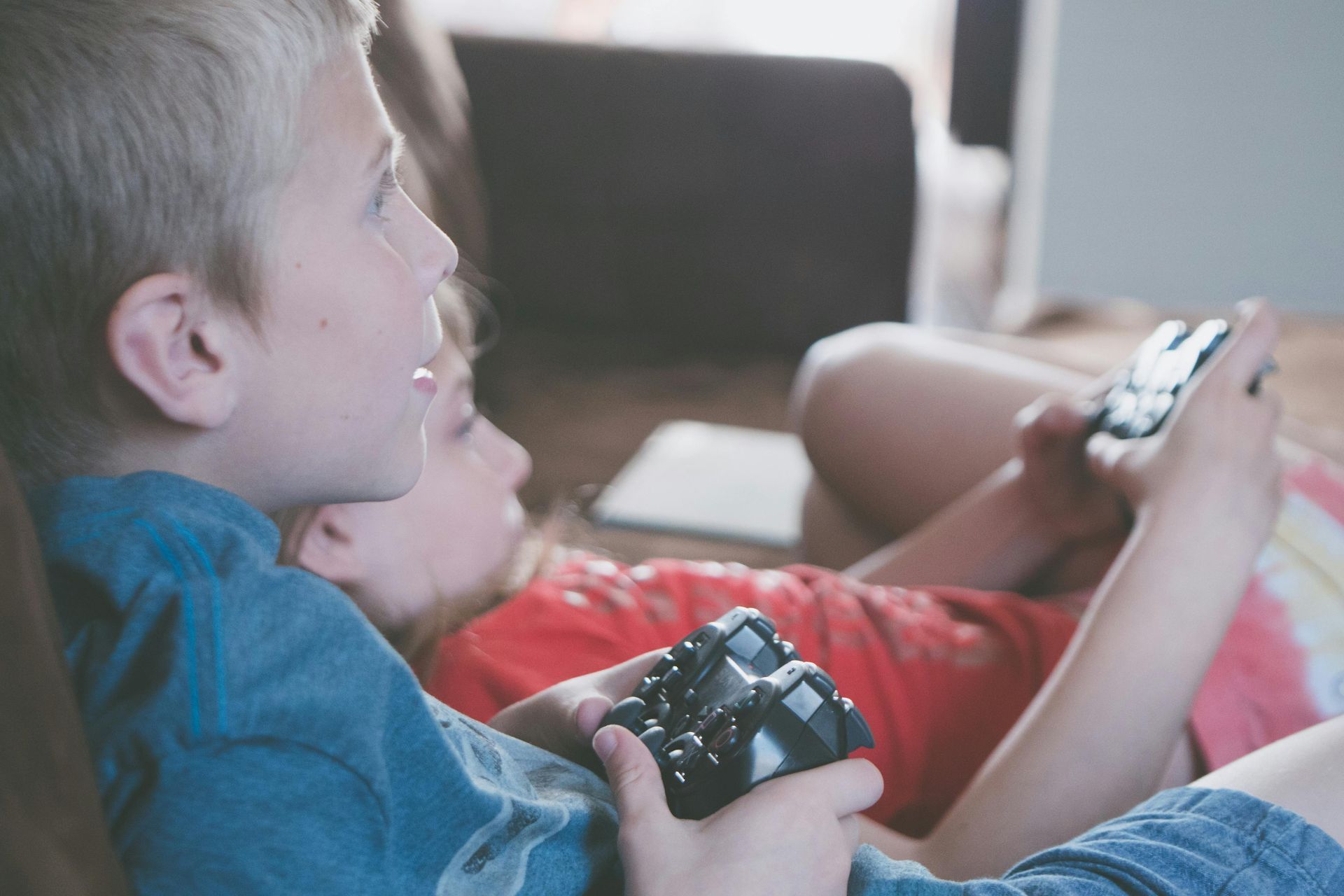 Two young boys are sitting on a couch playing a video game.