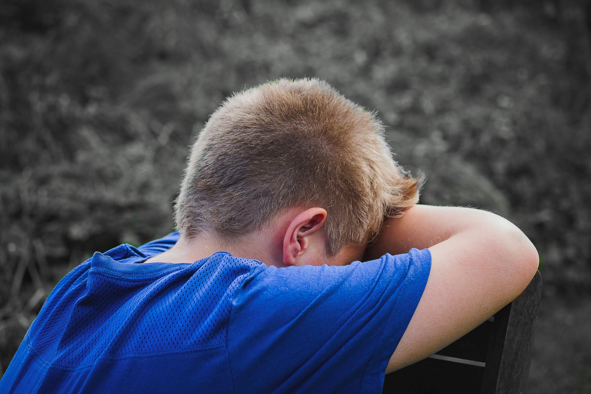 Person in blue shirt with head resting on arms, appearing sad.