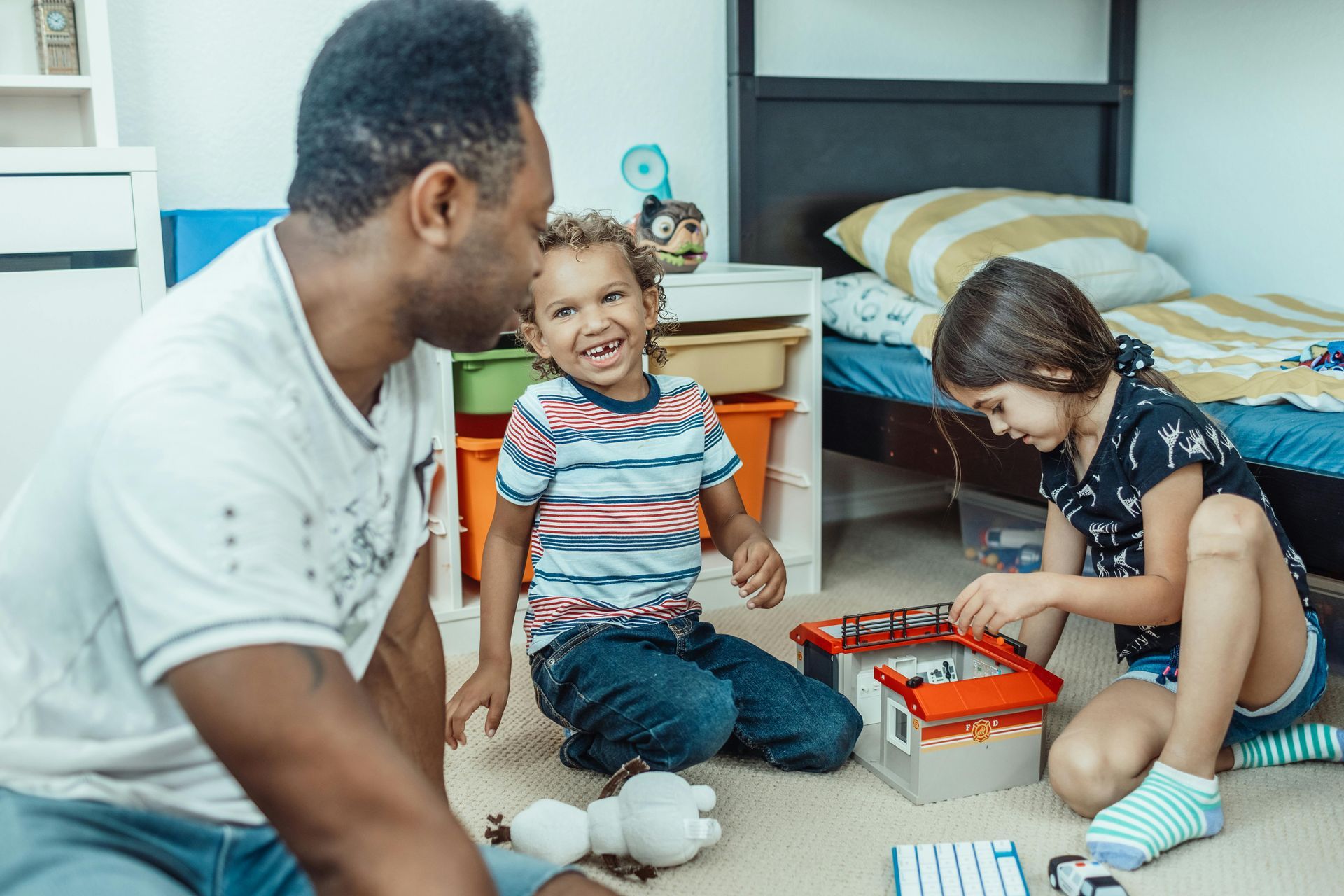 Man playing with two children in a child's bedroom with toys.