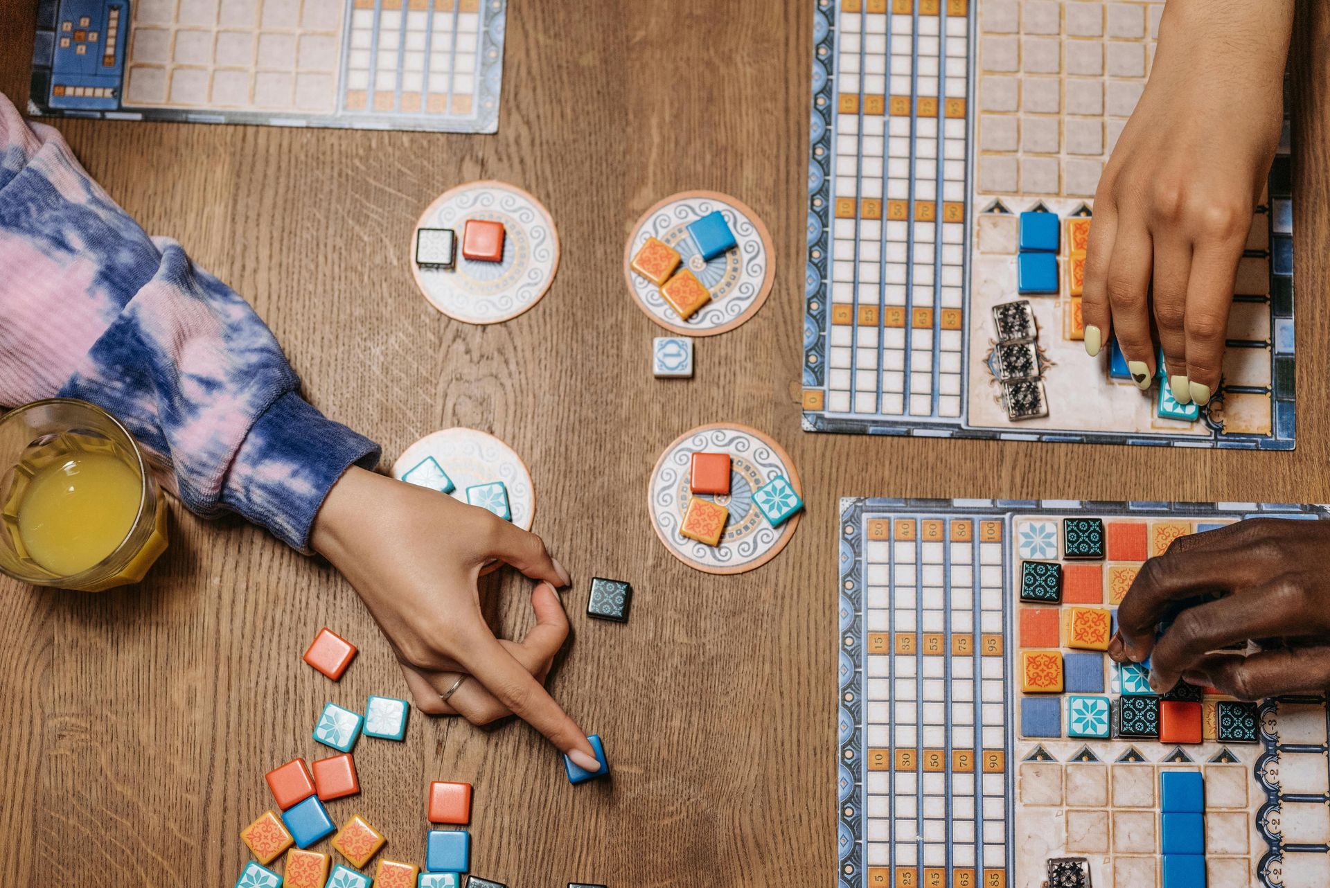 Kids and adults play a board game together on a wooden table, smiling and engaged in play.