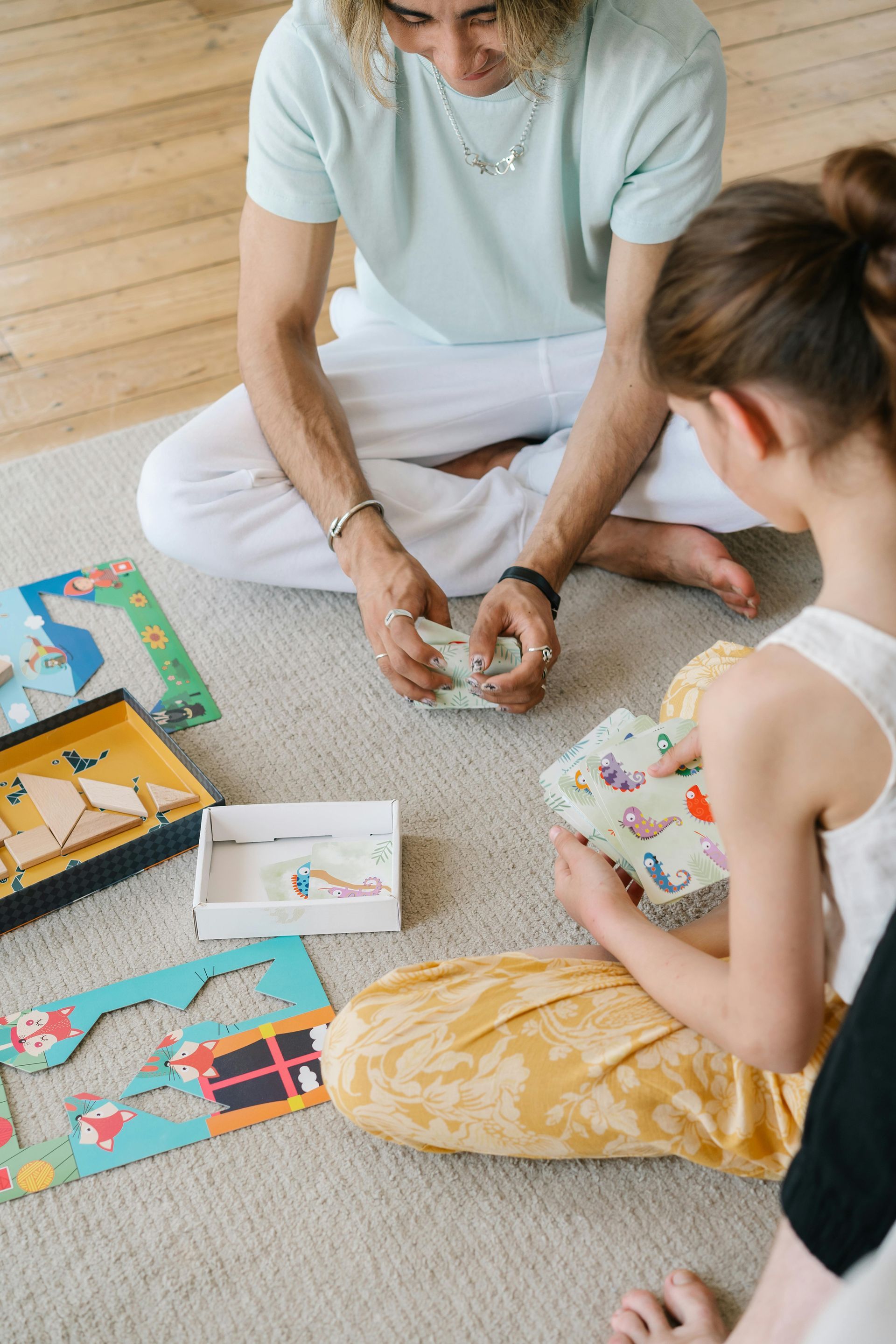 Person and child playing a game on the floor. Jigsaw puzzle pieces, various colors.
