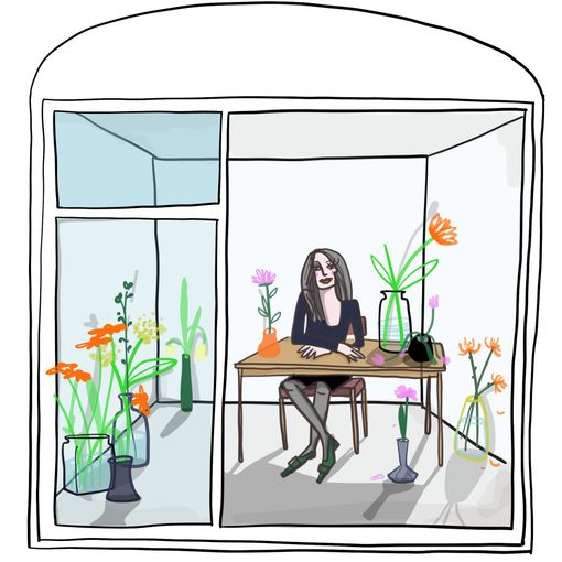 Art historian Tanja Pol sitting on a table in a room filled with beautiful flowers. She sits calmly with crossed legs 