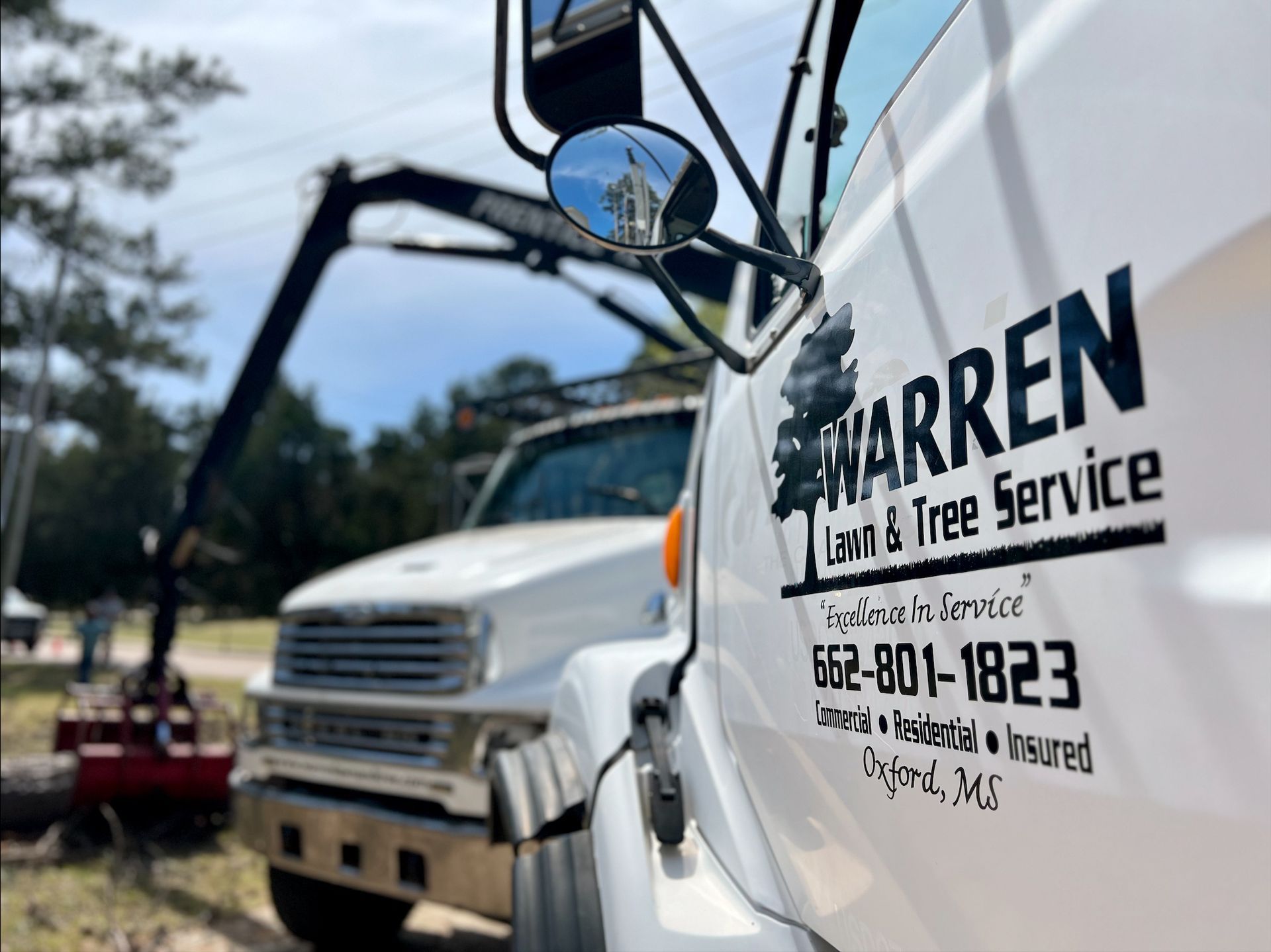 White Warren Lawn & Tree Service truck with boom arm, phone number, and logo.