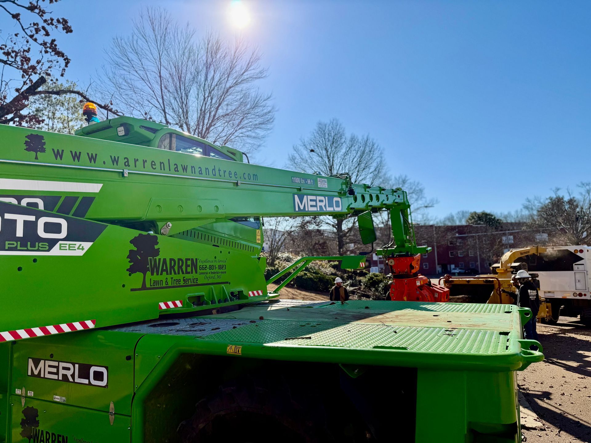 Green Merlo telehandler working, bright sunny day.