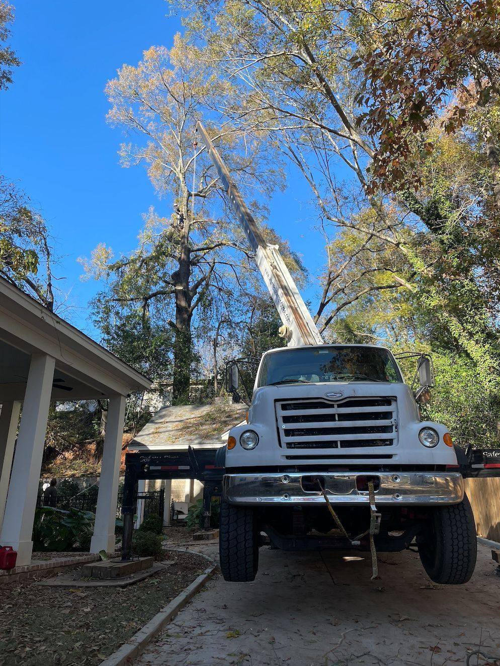 Truck with boom extending upward to trim a tree near a house; blue sky.
