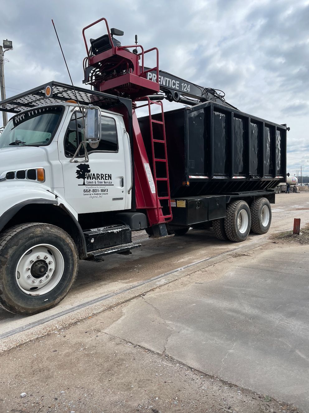 White dump truck with red ladder and aerial lift. Black dump bed. Cloudy sky.