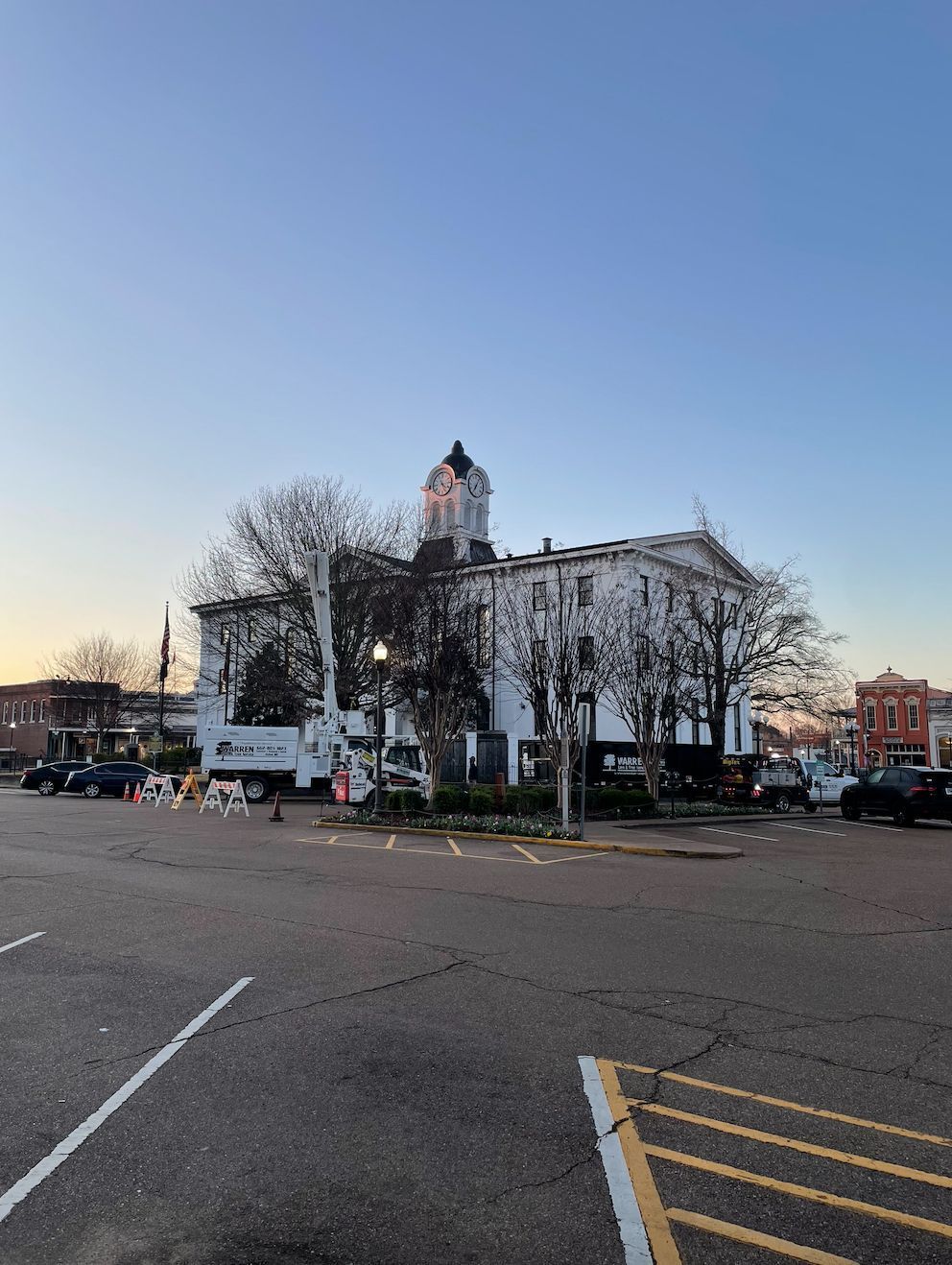 White courthouse building at dusk, with trees and parked cars in front.