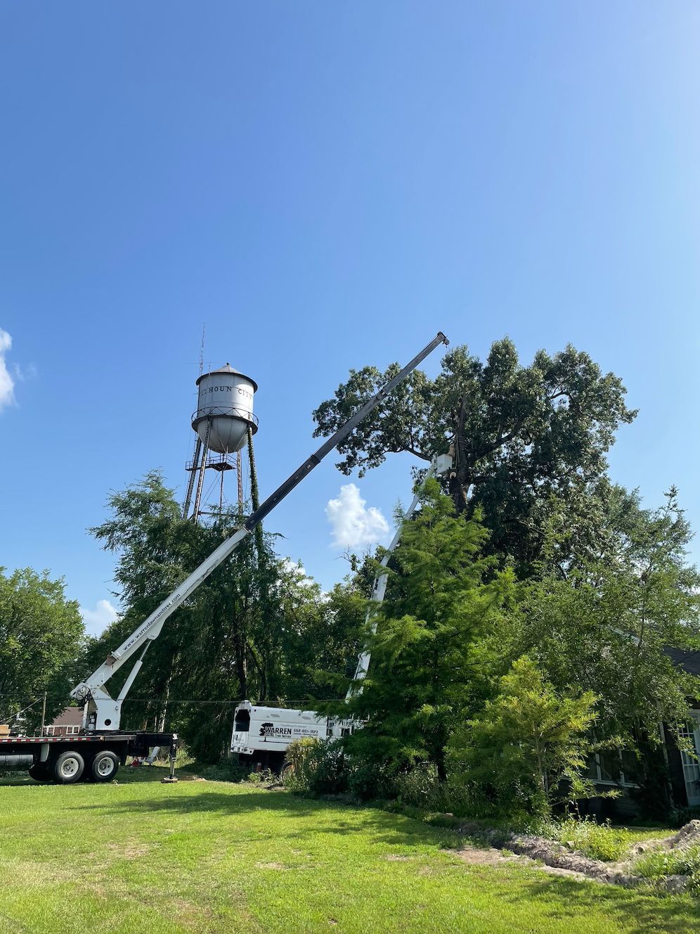 Tree trimming with crane near a water tower on a sunny day.
