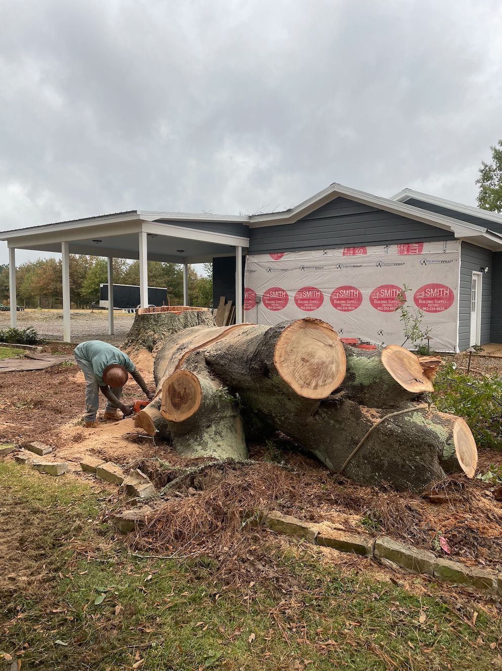 A person cutting a large tree stump in front of a house under construction.