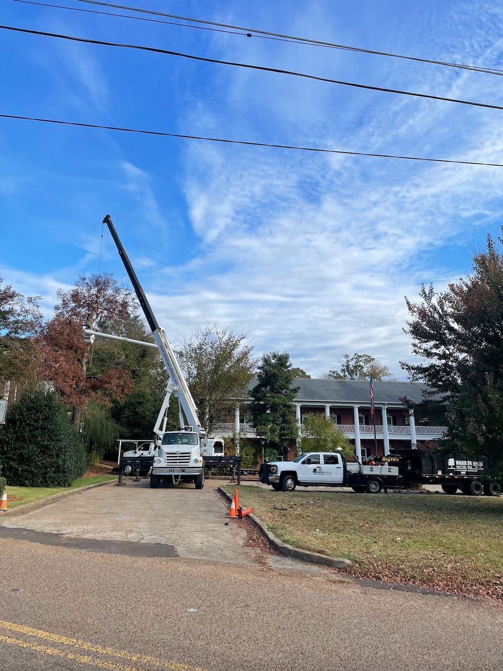 A utility truck with an extended boom working on power lines in front of a house. Blue sky overhead.